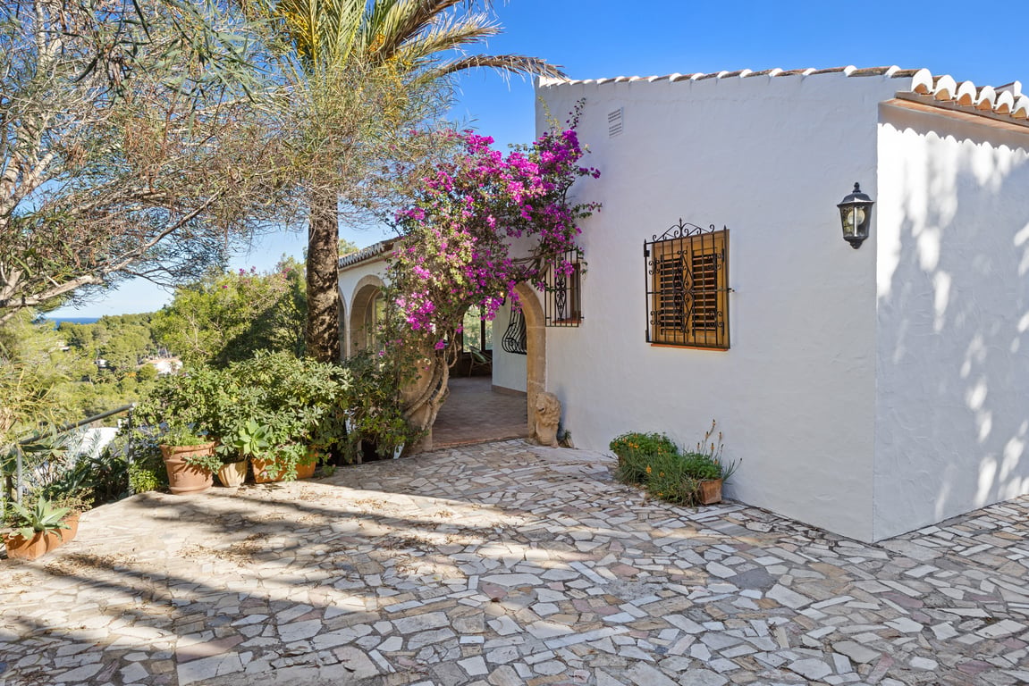 Traditionelle weiße Fassade mit Tosca-Steinbögen, blühender Bougainvillea und einer Natursteinterrasse mit Blick auf die Landschaft von Jávea.