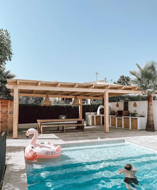 Außen-Essbereich und Sommerküche mit Pizzaofen und Grill unter einer Holzpergola, direkt neben dem Salzwasser-Pool gelegen.