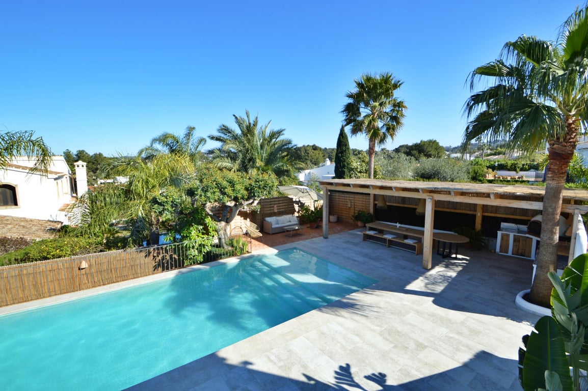 Erhöhte Ansicht des Salzwasserpools und der Steinterrasse mit einer Holzpergola, die einen Essbereich im Freien und eine Außenküche mit Pizzaofen umfasst.
