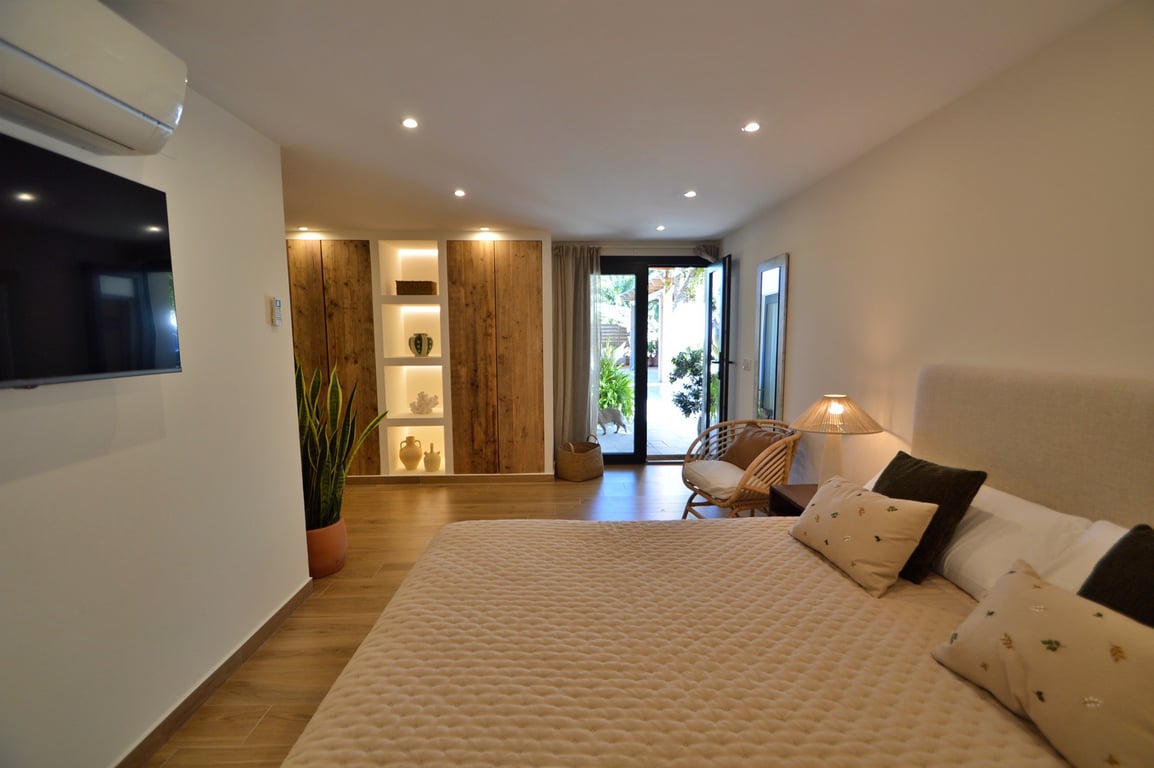 Helles Schlafzimmer mit Einbauschränken aus Naturholz, beleuchteten Regalen, Bodenfliesen in Holzoptik und direktem Zugang zur Terrasse.