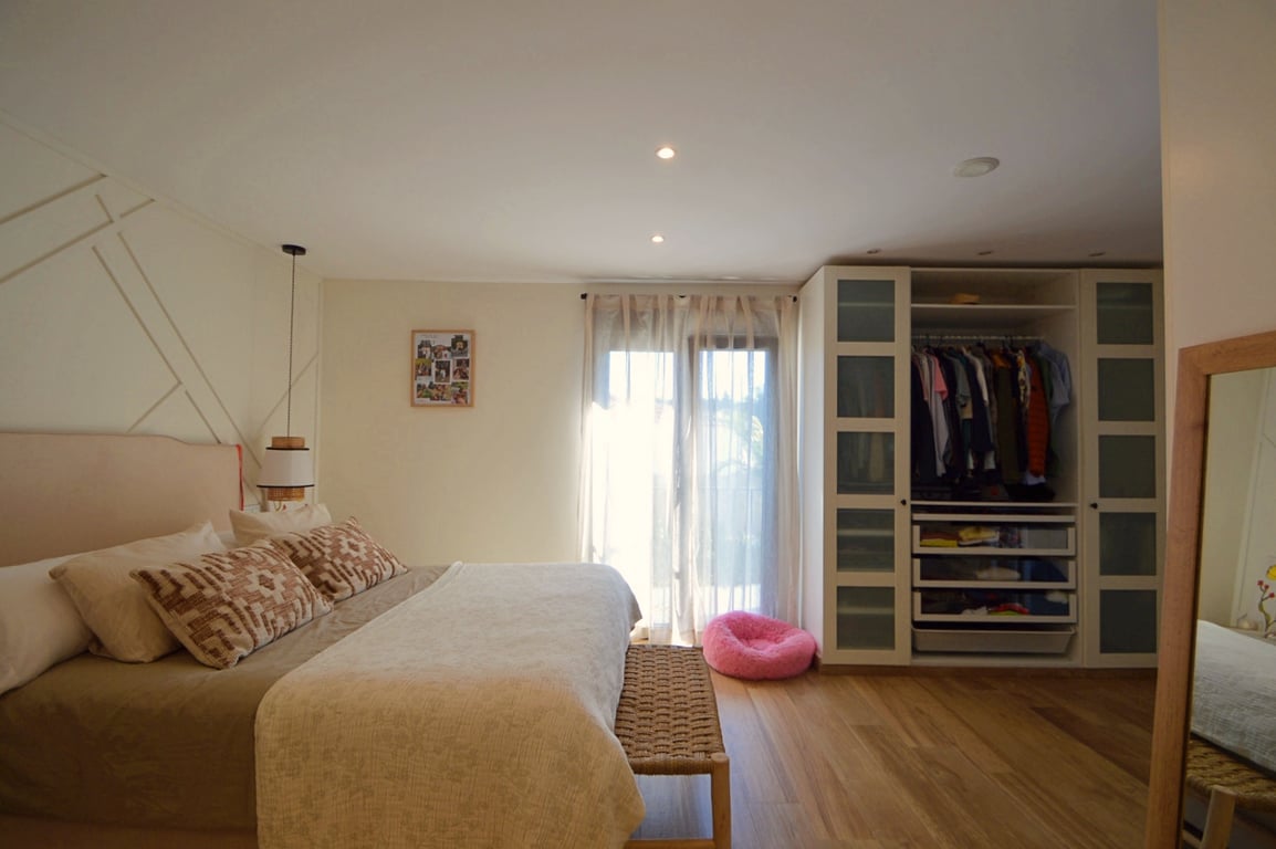Helles Schlafzimmer mit hellem Holzboden, geometrischer Akzentwand und Einbauschrank mit Milchglastüren und integrierten Regalsystemen.