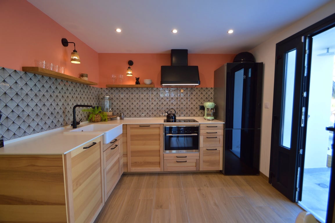 Moderne Küche mit hellen Holzschränken, weißem Spülstein und geometrischem Fliesenspiegel. Schwarze Elektrogeräte setzen Akzente vor der terrakottafarbenen Wand und Einbauspots.