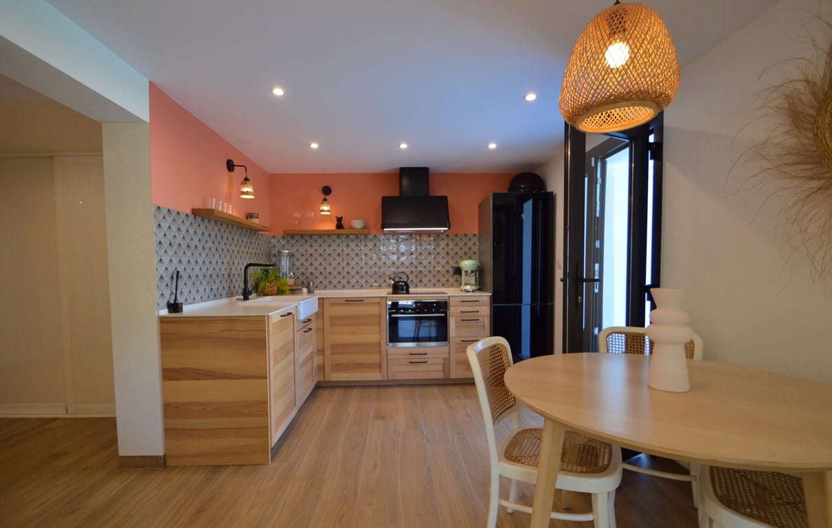Moderne Küche mit Holzschränken, terracottafarbener Akzentwand und Essbereich mit rundem Tisch, Wiener-Geflecht-Stühlen und einer Pendelleuchte aus Naturfasern.