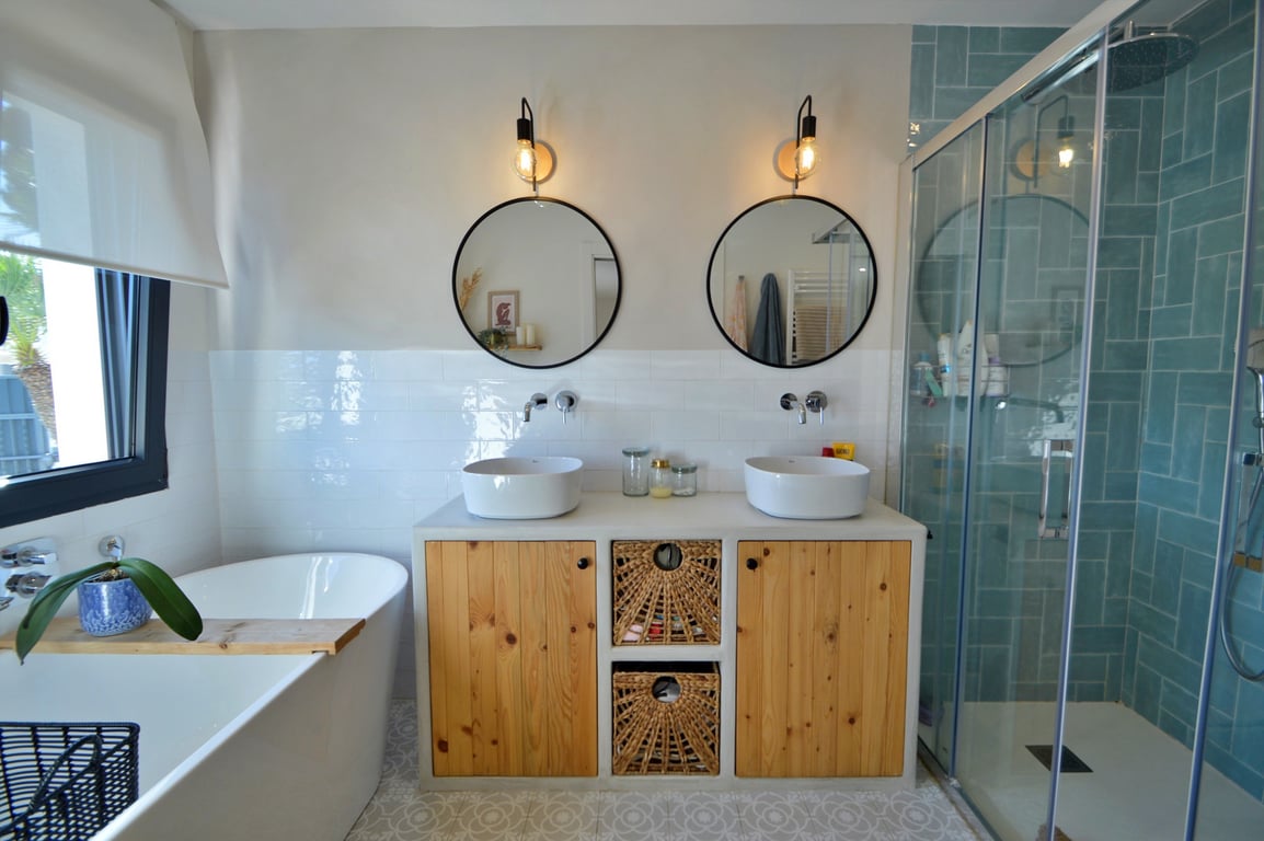 Modernes Badezimmer mit Doppelwaschtisch, Holzschränken, freistehender Badewanne und einer begehbaren Dusche mit markanten türkisfarbenen Fliesen.