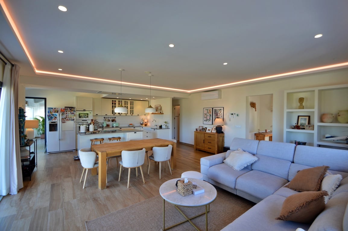 Offener Wohn- und Essbereich mit moderner Einbauküche, indirekter LED-Deckenbeleuchtung, hellem Parkettboden und zeitgenössischem Interieur.