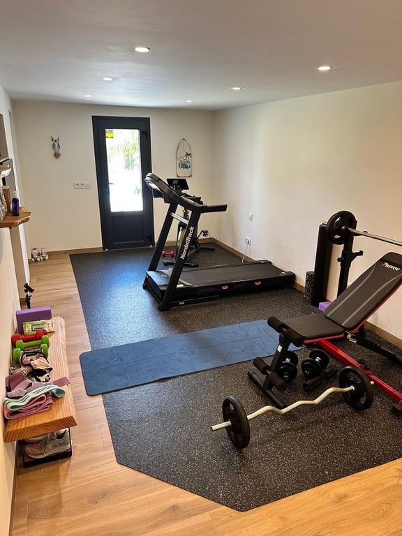 Privater Fitnessraum mit Laufband, Hantelbank und Yoga-Bereich, ausgestattet mit Holzeffektboden, Einbaustrahlern und direktem Außenzugang.