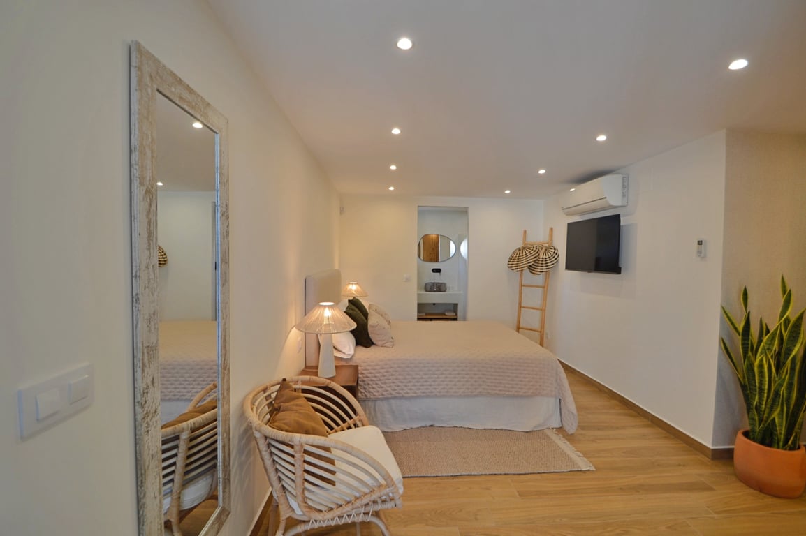 Schlafzimmer im ibizenkischen Stil mit Holzboden, LED-Einbaustrahlern, Klimaanlage und offen gestaltetem En-Suite-Badezimmer.
