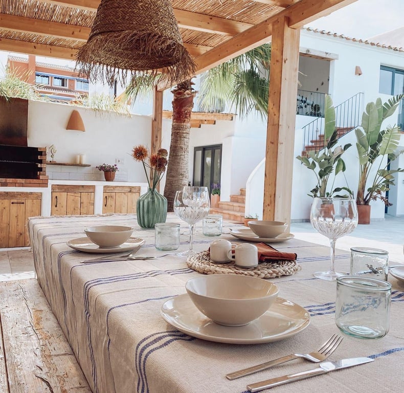 Überdachter Essbereich im Freien mit Holzpergola und Schilfdach, angrenzend an eine Außenküche mit gemauertem Grill im ibizenkischen Stil.