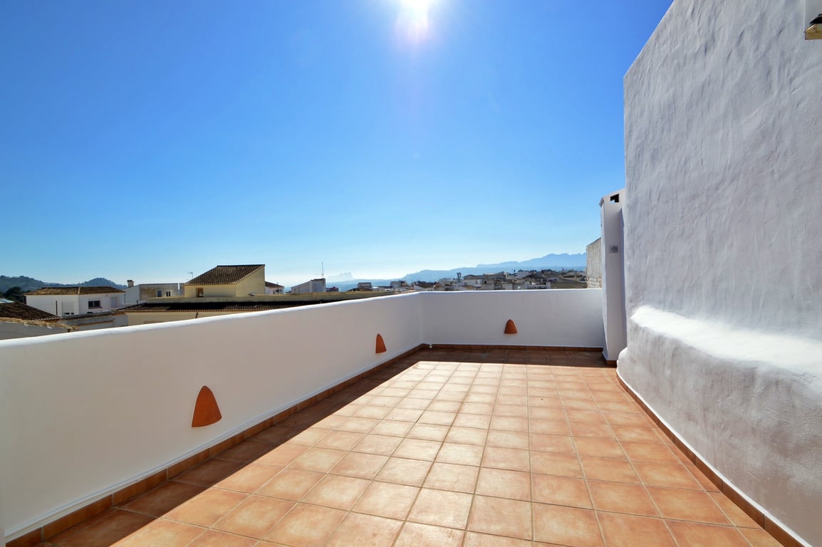 Dachterrasse mit Terrakotta-Fliesen und weißen Mauern, die einen weiten Panoramablick über das Dorf und die angrenzenden Berge bietet.
