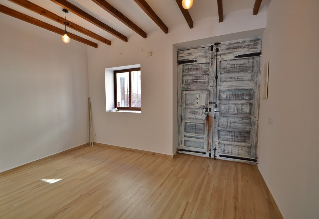 Haupteingang mit restaurierter rustikaler Holztür, sichtbaren Deckenbalken und hellem Holzboden in einem minimalistischen, lichtdurchfluteten Raum.