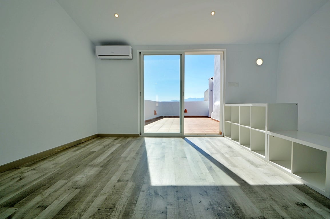 Heller Innenraum mit Laminatboden, Klimaanlage und Glasschiebetür, die direkt auf die großzügige Dachterrasse mit Bergblick führt.
