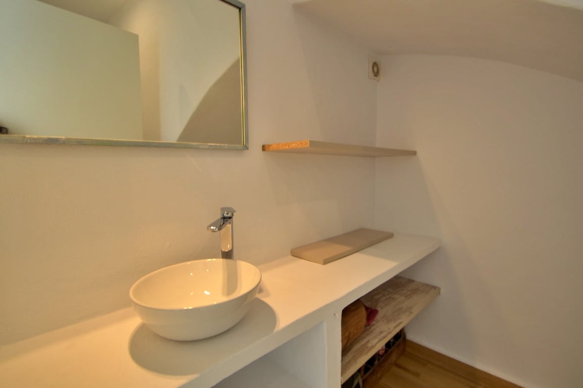 Minimalistisches Badezimmer mit Aufsatzwaschbecken auf weißem Waschtisch, offenen Regalen und rechteckigem Spiegel. Helle Wände und Holzakzente schaffen eine klare Optik.