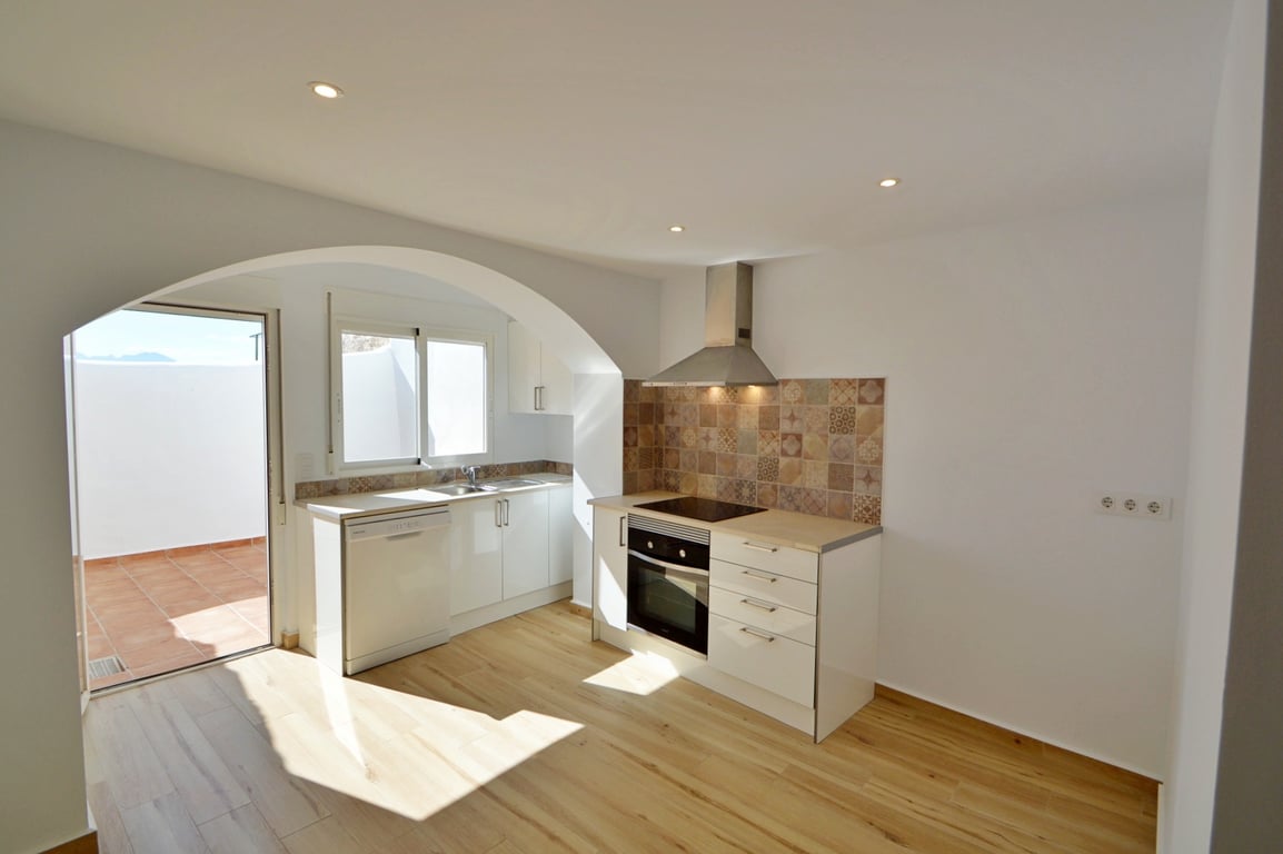 Modern renovierte Küche mit weißen Schränken, gemustertem Fliesenspiegel und direktem Zugang zu einem sonnigen privaten Innenhof.