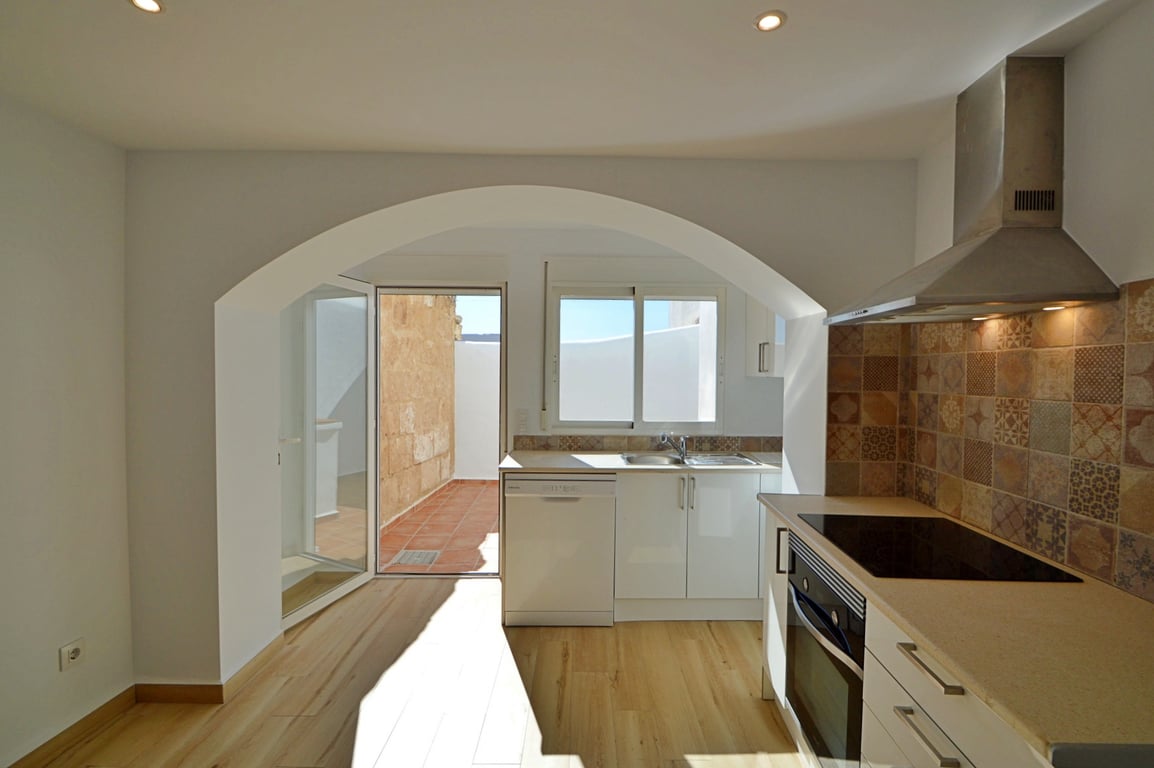 Moderne Küche mit markantem Rundbogen, dekorativem Fliesenspiegel und direktem Zugang zum privaten Innenhof mit traditionellen Terrakotta-Fliesen.