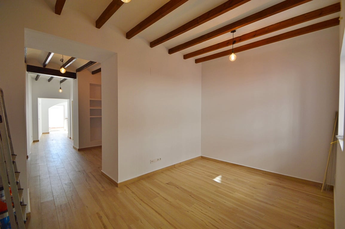 Offener Raum mit sichtbaren Holzbalken, hellem Bodenbelag und weißen Wänden. Pendelleuchten und natürliches Licht unterstreichen das renovierte, traditionelle Design.