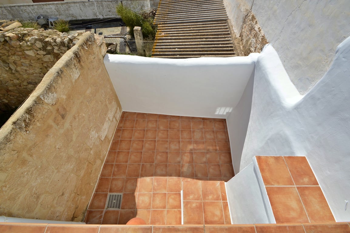 Private Terrasse mit Terrakotta-Fliesen, weiß getünchten Wänden und einer originalen Natursteinmauer, die den rustikalen Charme der Immobilie betont.