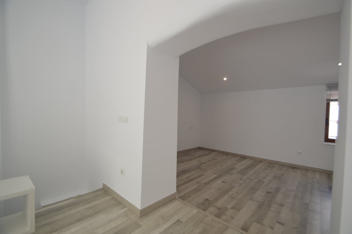 Renovierter Innenraum mit hellem Laminatboden, weißen Wänden und Deckeneinbaustrahlern. Der Raum bietet einen breiten Durchgang und ein Fenster mit dunklem Rahmen.