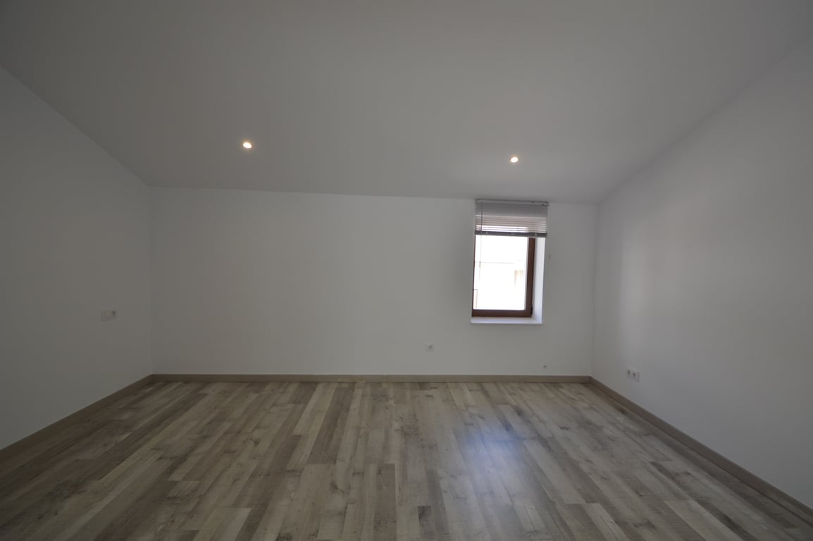 Renovierter Raum mit hellem Laminatboden, glatten weißen Wänden, Deckeneinbaustrahlern und einem Fenster mit Jalousie.
