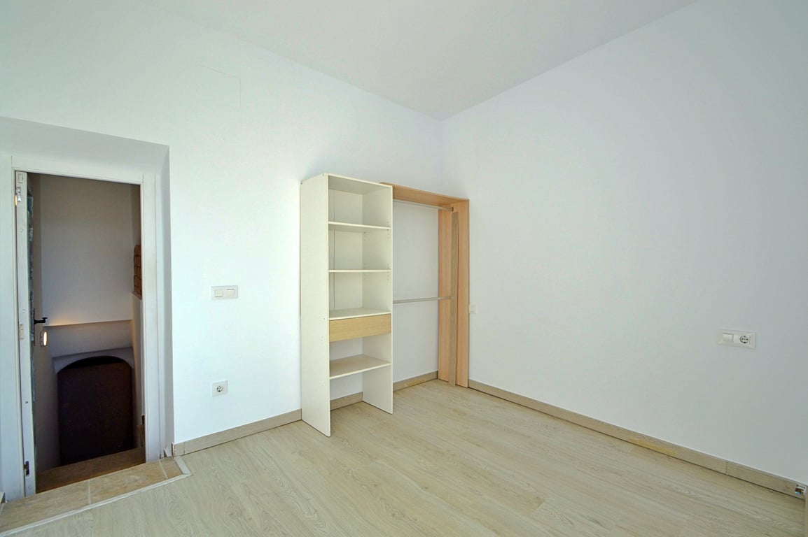 Vielseitiger Raum mit Bodenfliesen in Holzoptik, weißen Wänden und einem offenen Regalsystem mit Kleiderstange neben dem Treppenaufgang.