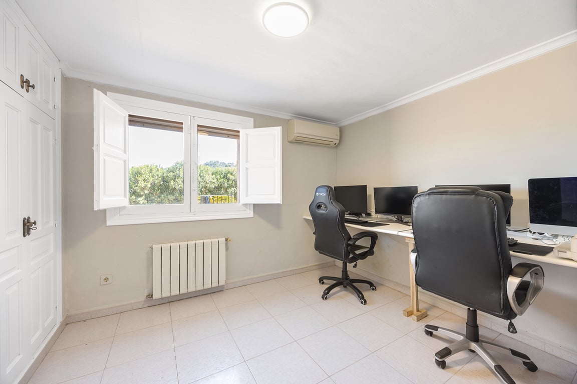 Helles Arbeitszimmer mit Einbauschränken, Klimaanlage und Heizkörper. Das Fenster mit Innenläden bietet Tageslicht und einen Blick ins Grüne auf dem weitläufigen Grundstück.