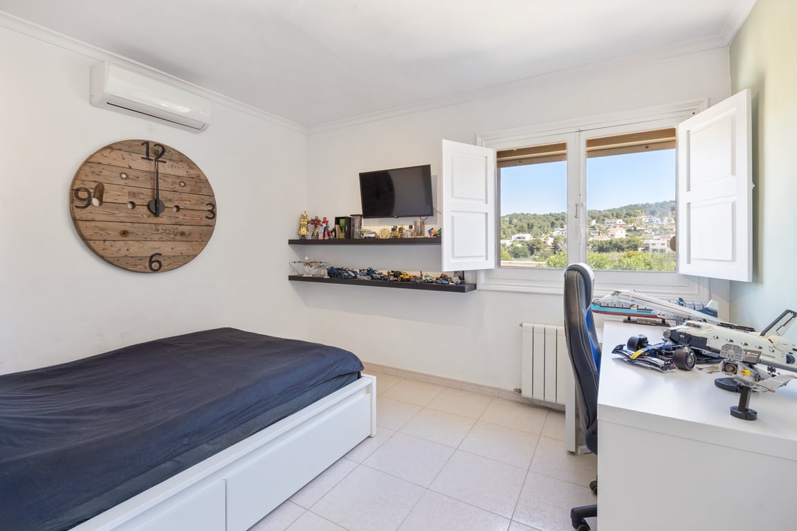 Helles Schlafzimmer mit Klimaanlage, Arbeitsbereich und Fenster mit weißen Fensterläden, das einen weiten Blick auf die Hügellandschaft bietet.