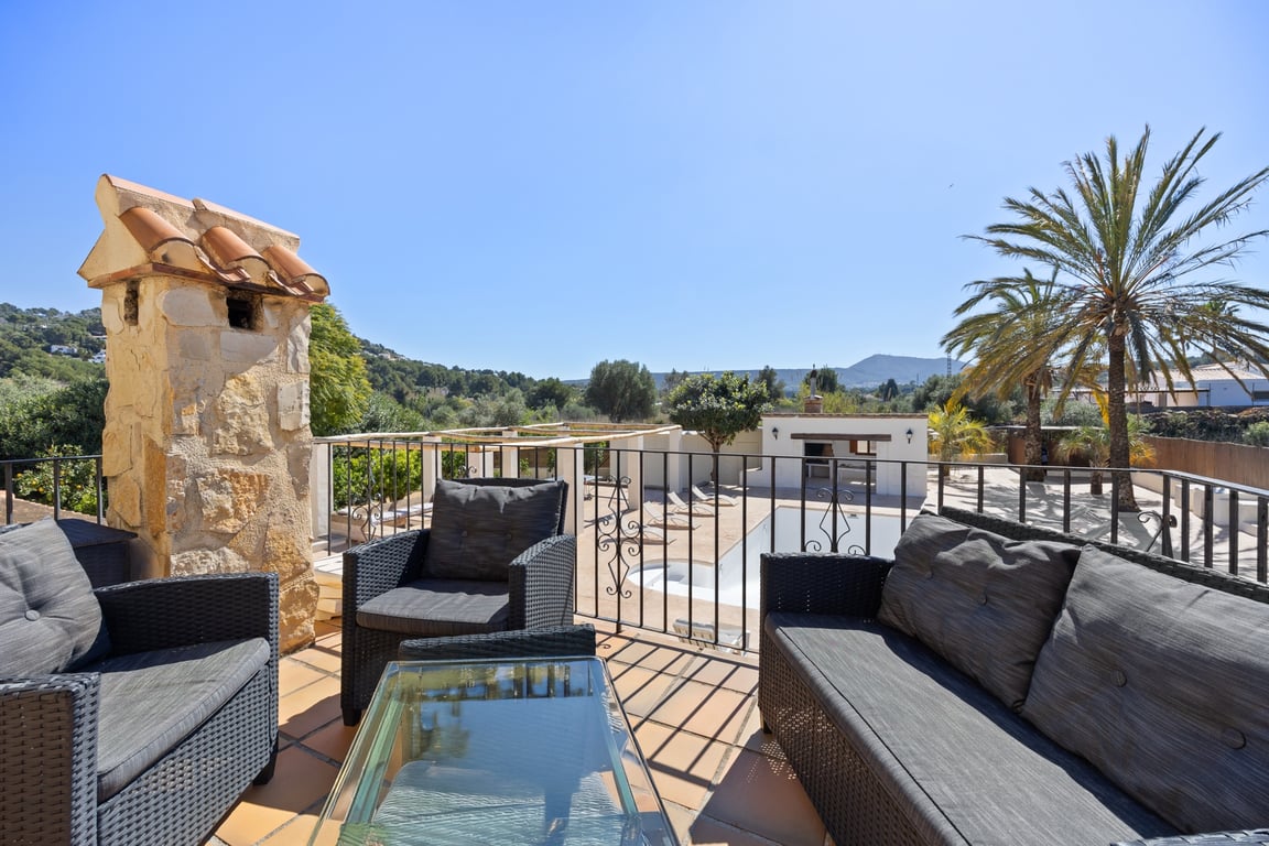 Obere Terrasse mit Rattan-Sitzgruppe, Terrakottaboden und Blick auf den Poolbereich, die Außenküche und die umliegende Hügellandschaft von Jávea.