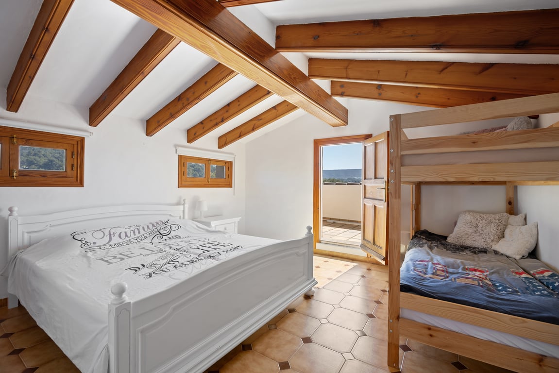 Schlafzimmer im Dachgeschoss mit sichtbaren Holzbalken, Terrakottaboden und Zugang zur privaten Terrasse. Ausgestattet mit einem Doppelbett und einem Etagenbett aus Holz.
