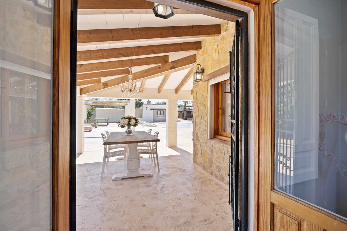 Überdachte Terrasse mit sichtbaren Holzbalken, Natursteinwänden und einem Essbereich im Freien mit Blick auf den Poolbereich.