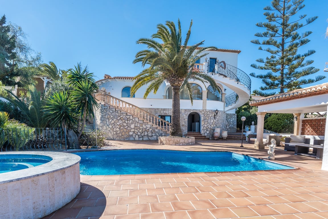 Außenansicht mit Swimmingpool, rundem Whirlpool und Steinfassade. Eine markante Wendeltreppe verbindet die Terrassenebenen inmitten mediterraner Bepflanzung.