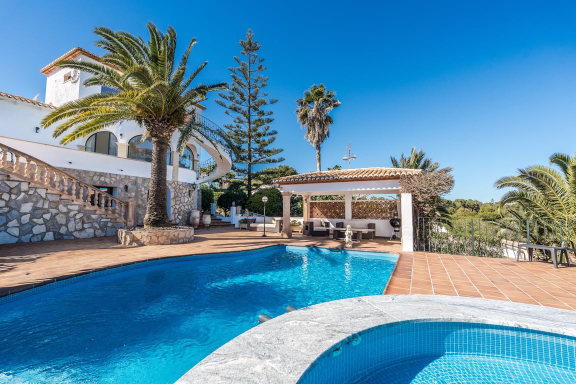 Außenbereich mit Pool und Jacuzzi, umgeben von einer Terrakotta-Terrasse, Palmen und einer Steinfassade mit klassischer Treppe und überdachter Lounge.