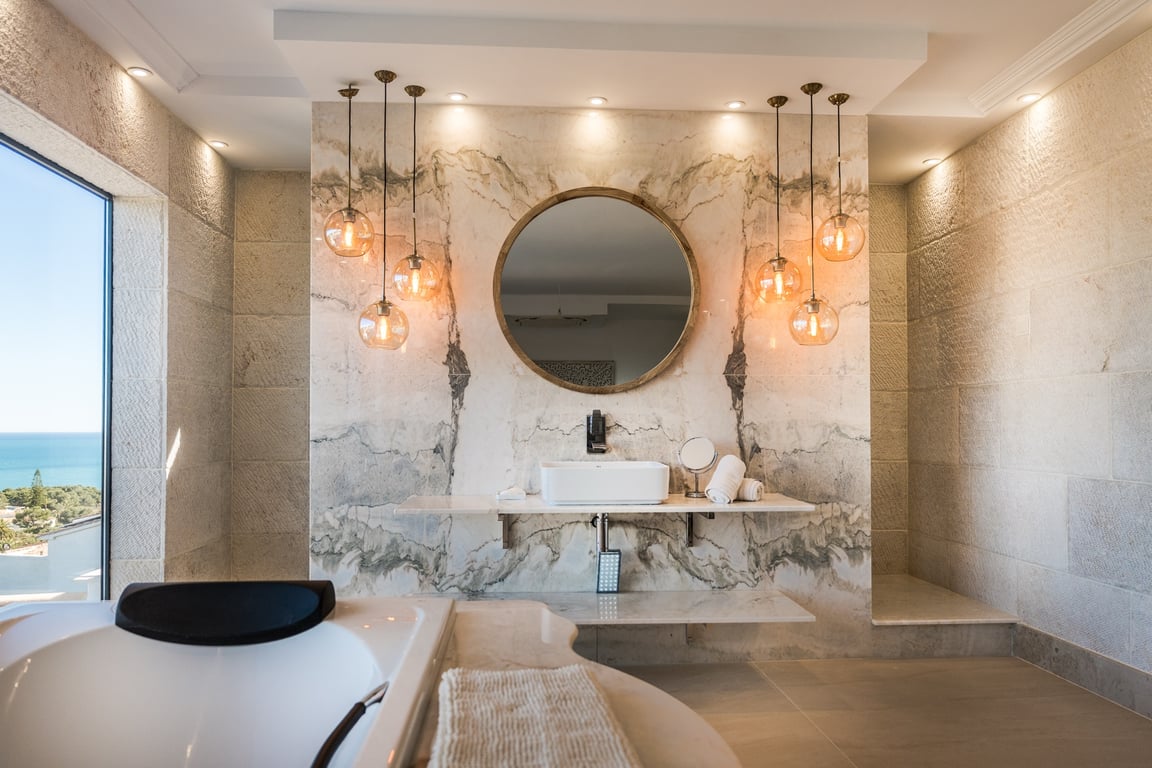Badezimmer der Master-Suite mit markanter Marmorwand, Aufsatzwaschbecken auf schwebendem Regal, Designer-Pendelleuchten und weitem Meerblick durch das Fenster.