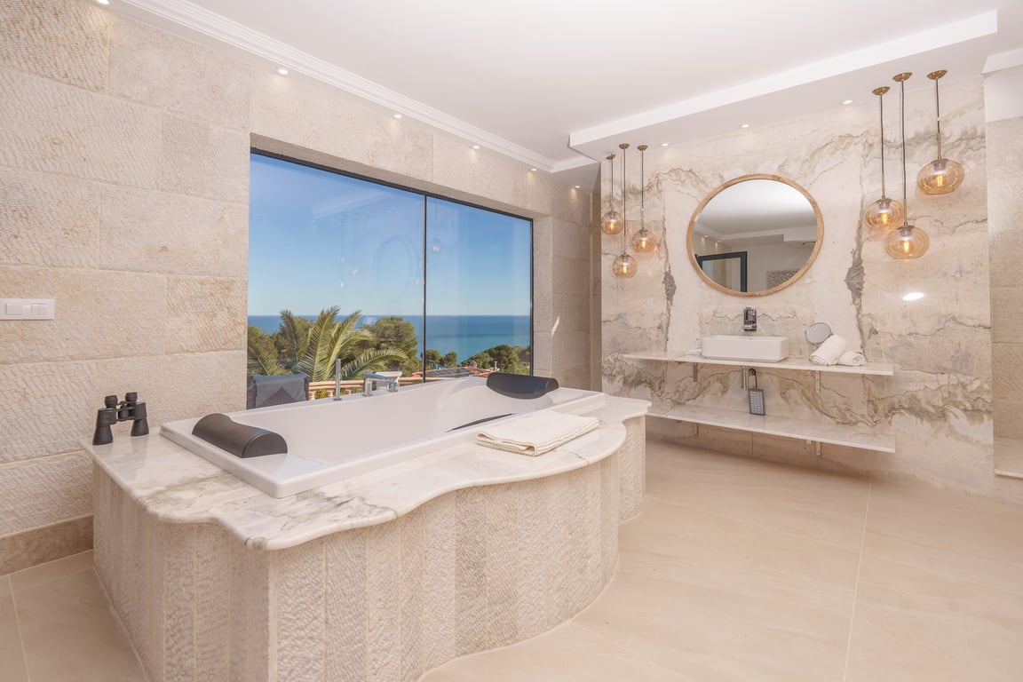 Badezimmer der Master-Suite mit marmorgefasster Badewanne, Kalksteinwänden und großem Fenster mit weitem Blick auf das Mittelmeer.