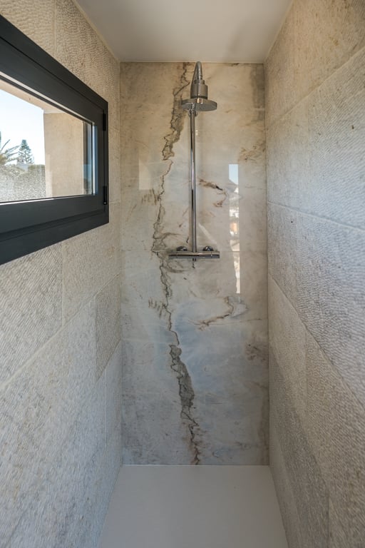 Begehbare Dusche mit einer Rückwand aus gemasertem Marmor und Seitenwänden aus strukturiertem Kalkstein. Ausgestattet mit Chromarmaturen und natürlichem Lichteinfall.