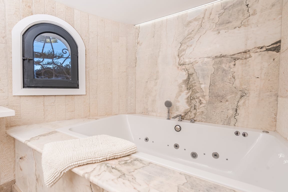 Einbau-Whirlpool mit edler Marmoreinfassung, strukturierten Natursteinwänden und einem charakteristischen Rundbogenfenster.