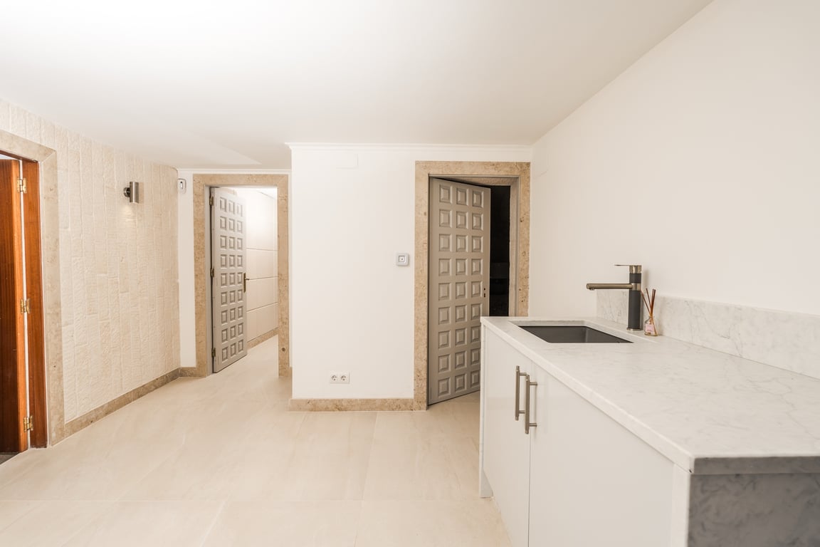Funktionaler Flurbereich mit Marmorarbeitsplatte und Spülbecken. Türrahmen aus Naturstein und dekorative graue Paneeltüren prägen das helle Interieur.