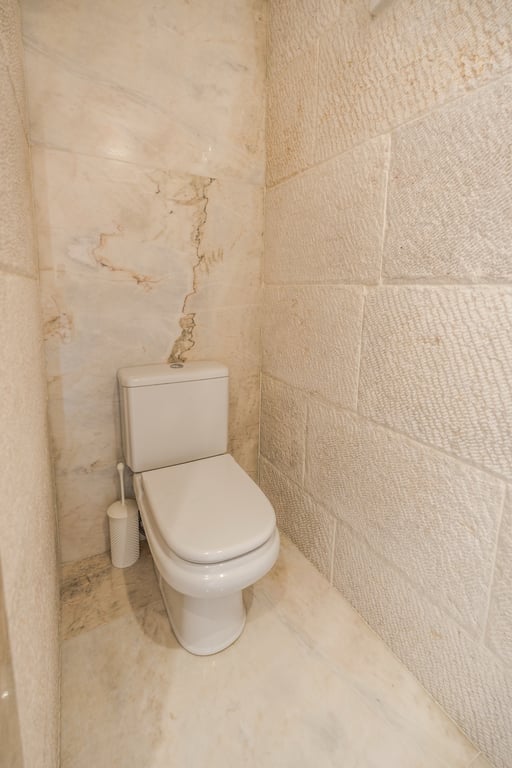 Gäste-WC mit Wänden aus strukturiertem Kalkstein und poliertem Marmor, die eine natürliche und zeitlose Atmosphäre schaffen.