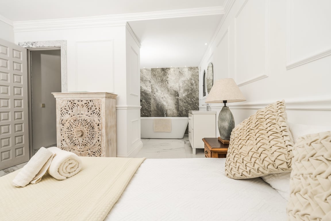 Hauptschlafzimmer mit offenem Badkonzept, freistehender Badewanne vor einer Marmorwand und klassischen Wandverzierungen.