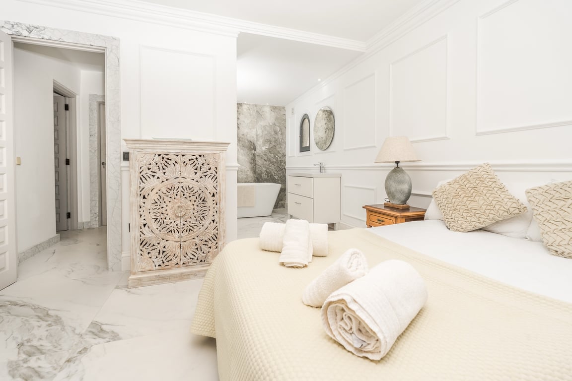 Master-Suite mit offenem Badezimmer, freistehender Badewanne und Natursteinwand. Marmorböden und klassische Wandleisten prägen das elegante, helle Design.