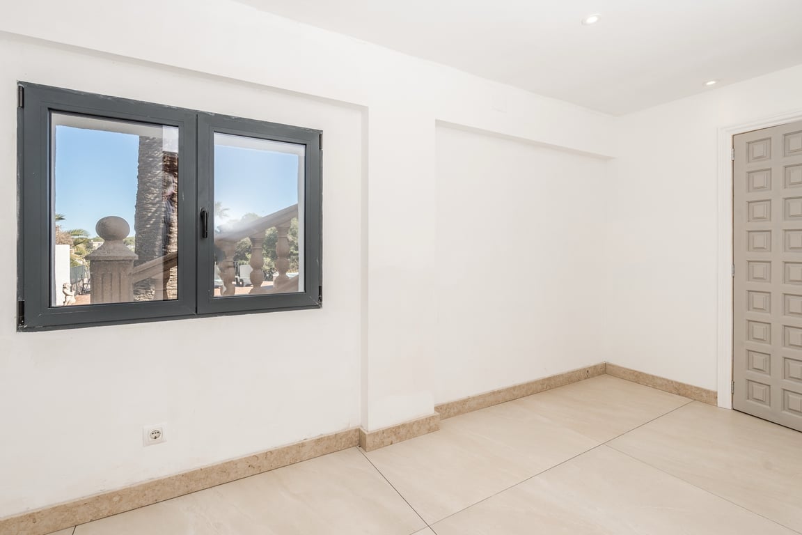 Renovierter Raum mit Natursteinboden, Deckeneinbaustrahlern und dunklem Aluminiumfenster mit Blick auf den Außenbereich der Villa.
