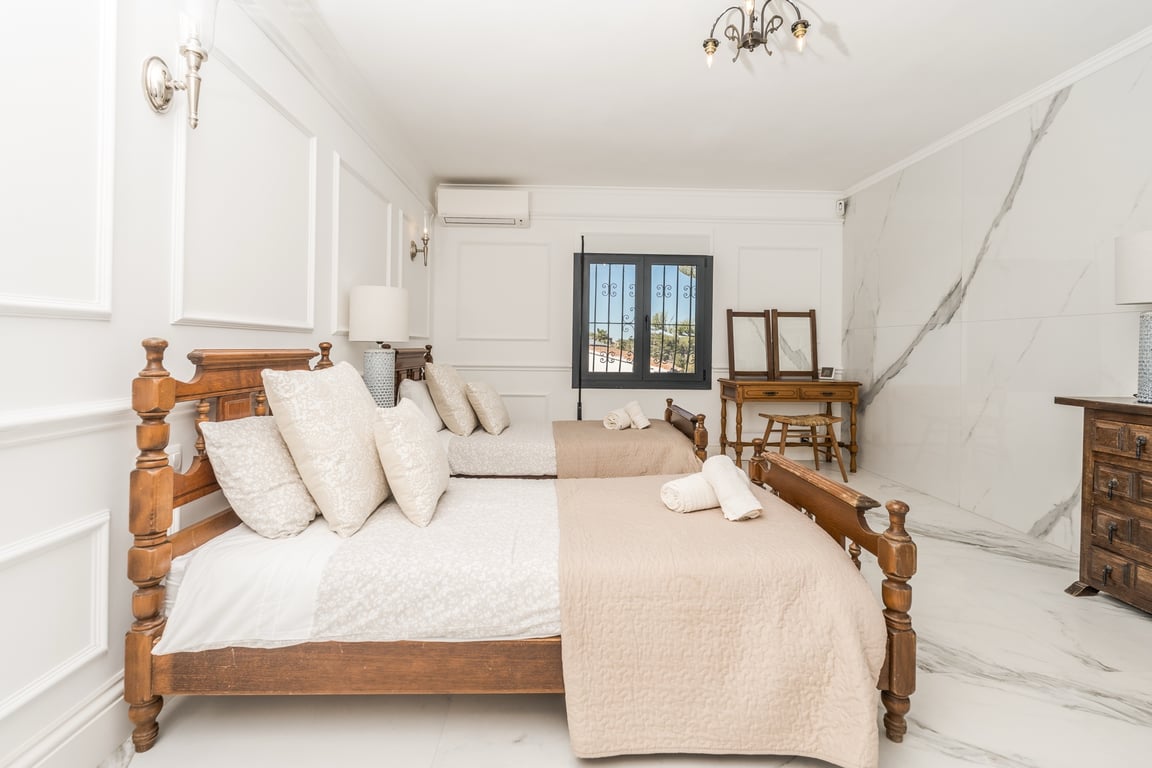 Schlafzimmer mit zwei Holzbetten, Marmorboden und klassischen Wandleisten. Ausgestattet mit einem rustikalen Schminktisch und Klimaanlage.
