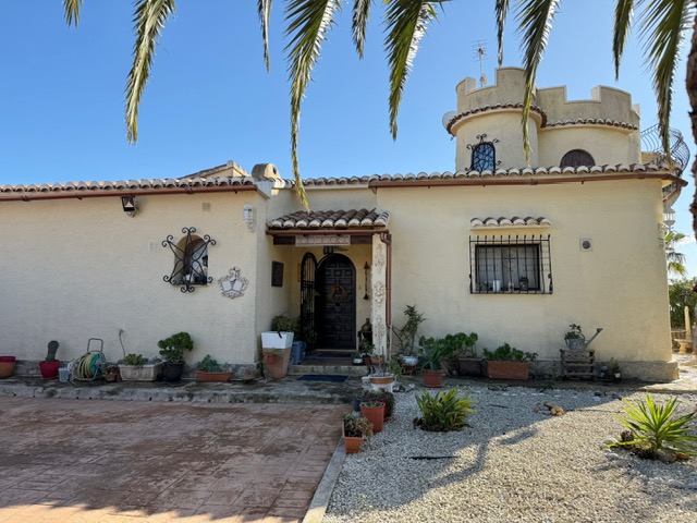 Außenansicht der Villa mit markantem Zinnenturm, Rundbogenfenstern mit Schmiedeeisengittern und einem Eingangsbereich mit mediterraner Bepflanzung.