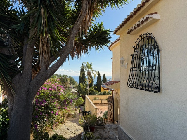 Außenfassade mit traditionellen schmiedeeisernen Gittern, umgeben von mediterraner Bepflanzung und weitem Blick auf das Meer.