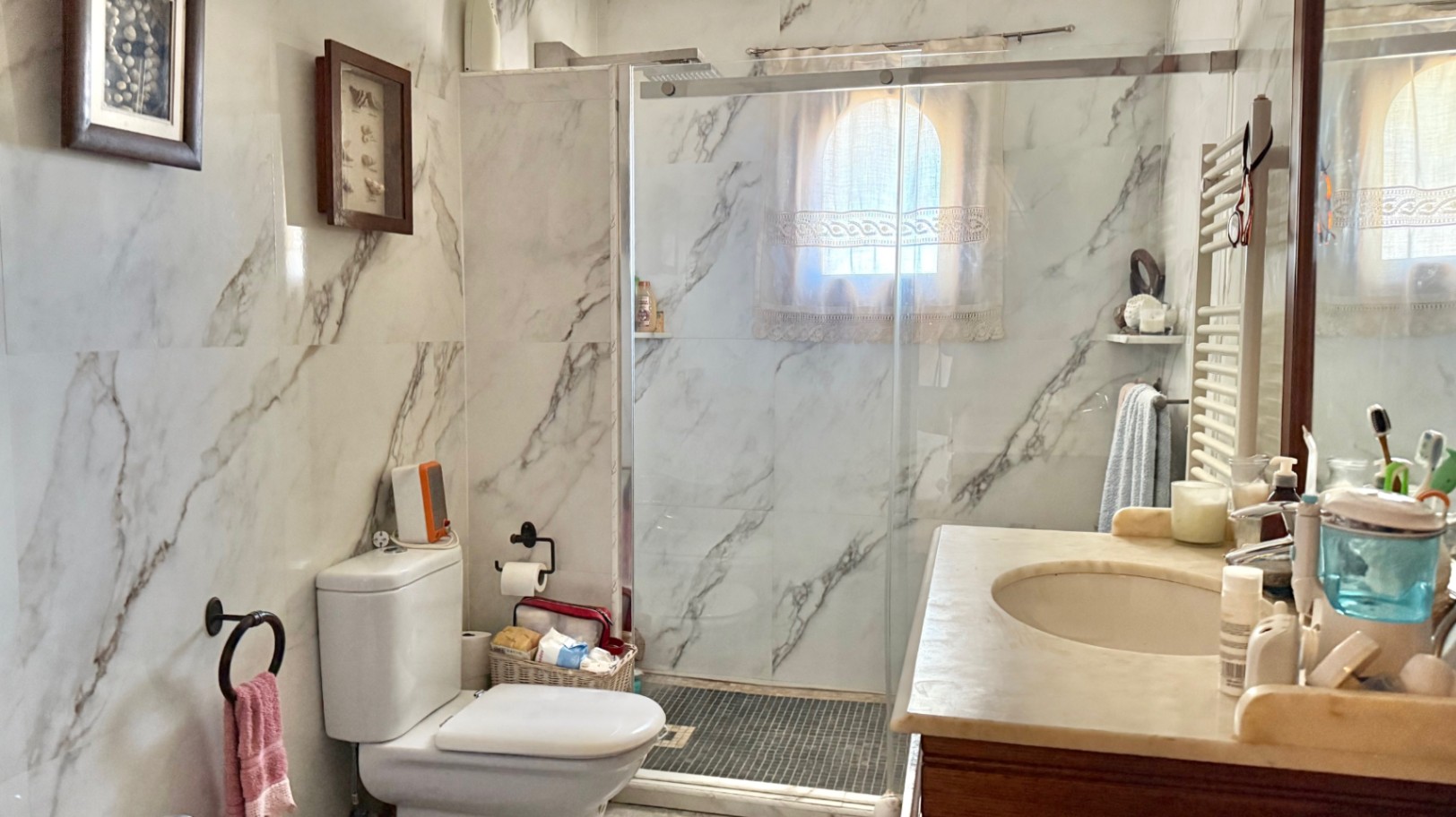 Badezimmer mit großformatigen Marmoroptik-Fliesen, ebenerdiger Dusche mit Glastrennwand und einem Waschtisch mit Natursteinplatte.