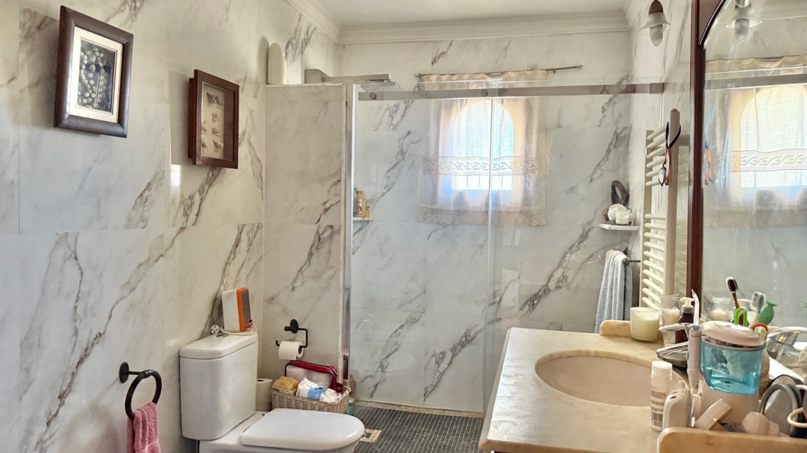Badezimmer mit marmorierten Wandfliesen, begehbarer Dusche mit Glastrennwand und einem kleinen Rundbogenfenster für natürliches Licht.