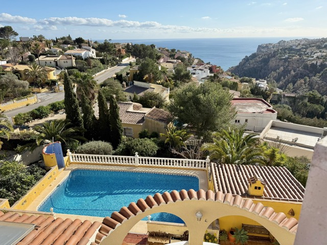 Erhöhte Ansicht des rechteckigen Pools mit weißer Balustrade, eingerahmt von bogenförmigen Ziegeldächern und weitem Blick auf das Mittelmeer und die Küste.