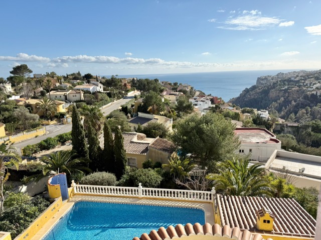 Erhöhter Blick auf den privaten Pool mit weißer Balustrade, die umliegende Wohngegend und das weite Mittelmeer am Horizont unter klarem Himmel.