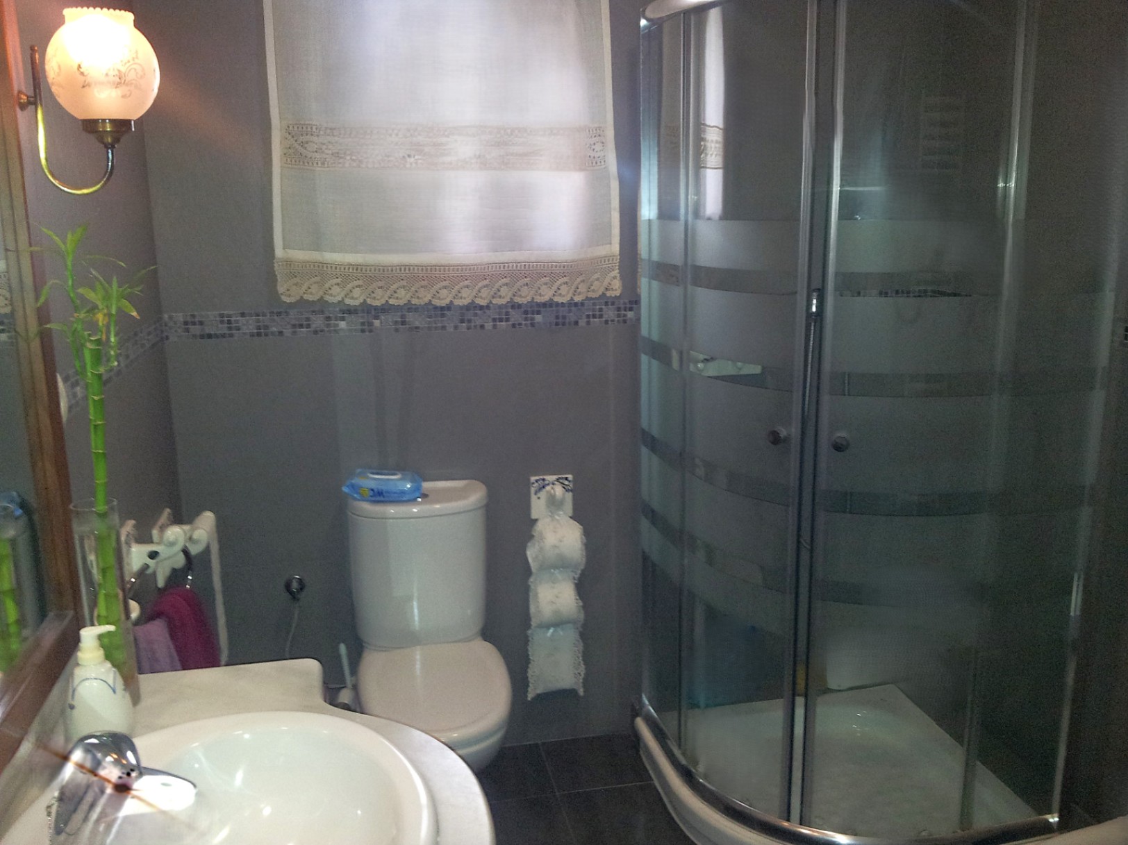 Funktionales Badezimmer mit Eckduschkabine, Marmor-Waschtisch und grauen Wandfliesen mit dekorativer Mosaikbordüre.