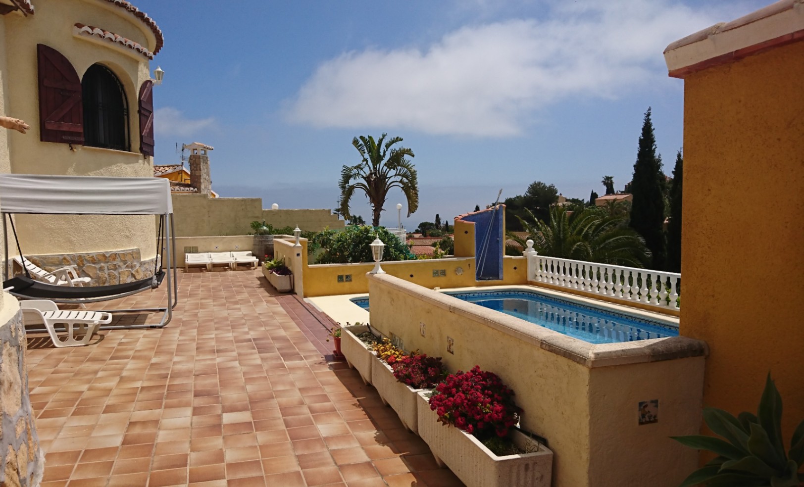 Großzügige Außenterrasse mit Terrakottafliesen, privatem Pool und einem charakteristischen Villenturm mit Holzfensterläden in sonniger Lage.