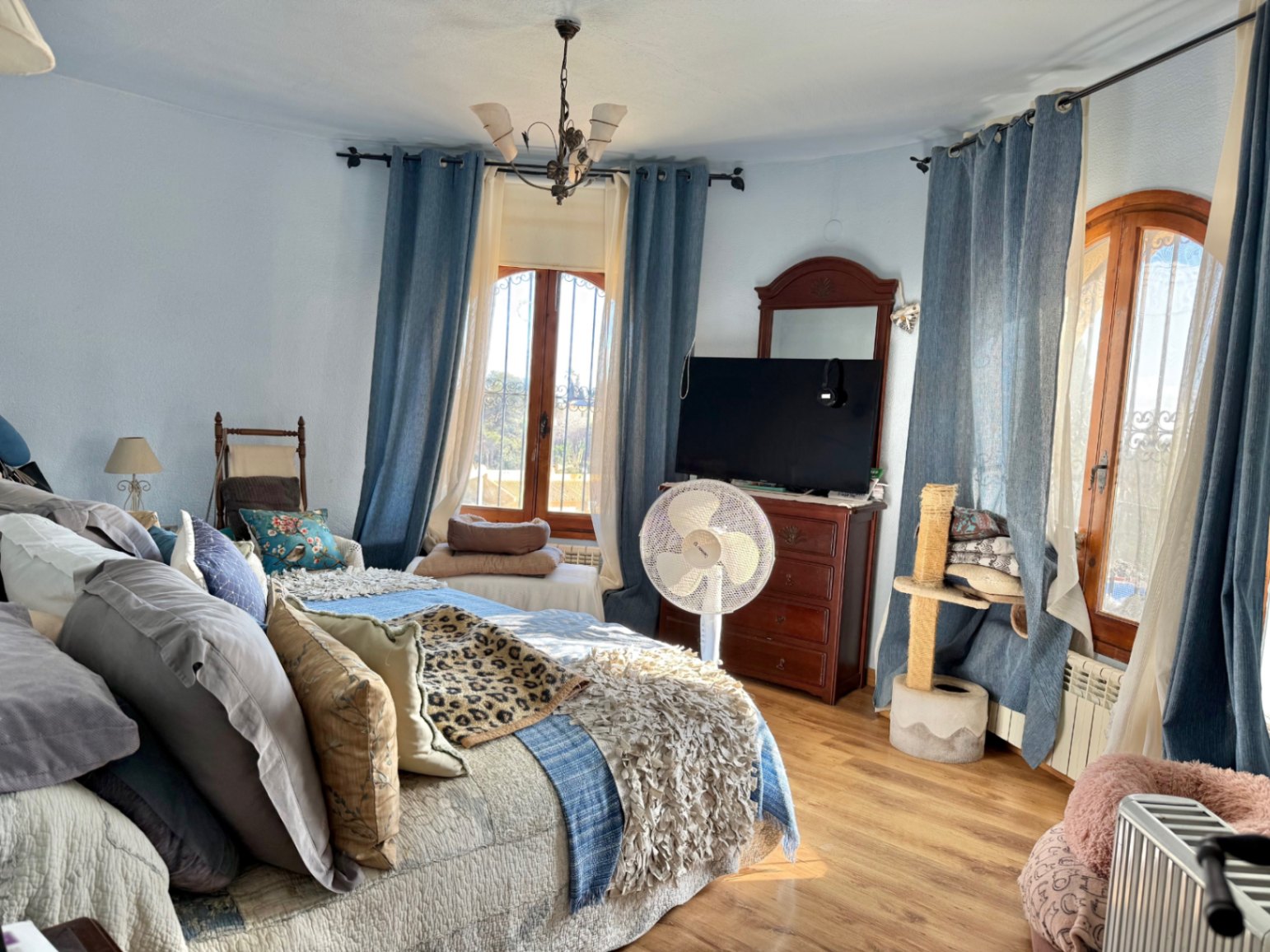 Helles Schlafzimmer mit geschwungener Wand, Rundbogenfenstern aus Holz und Laminatboden. Ausgestattet mit klassischen Holzmöbeln und viel natürlichem Licht.