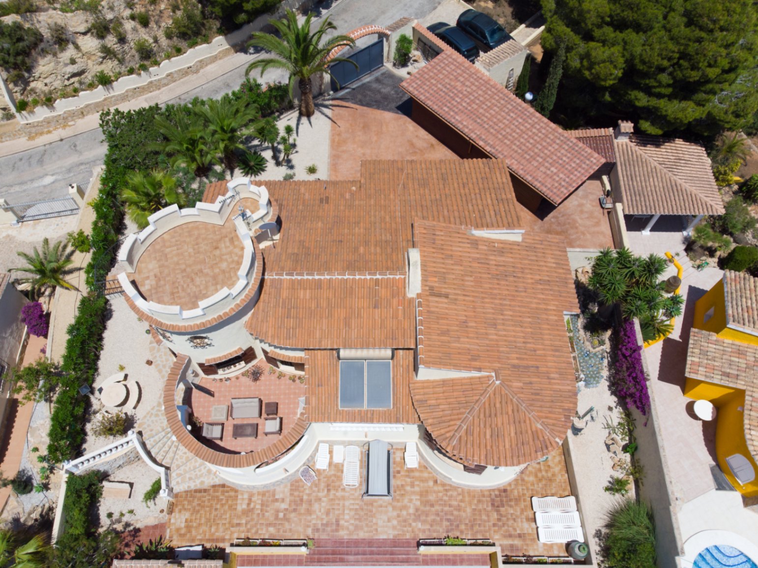 Luftaufnahme der Villa, die die mediterrane Architektur mit Ziegeldächern, einem markanten Rundturm, Sonnenkollektoren und weitläufigen Terrassen zeigt.